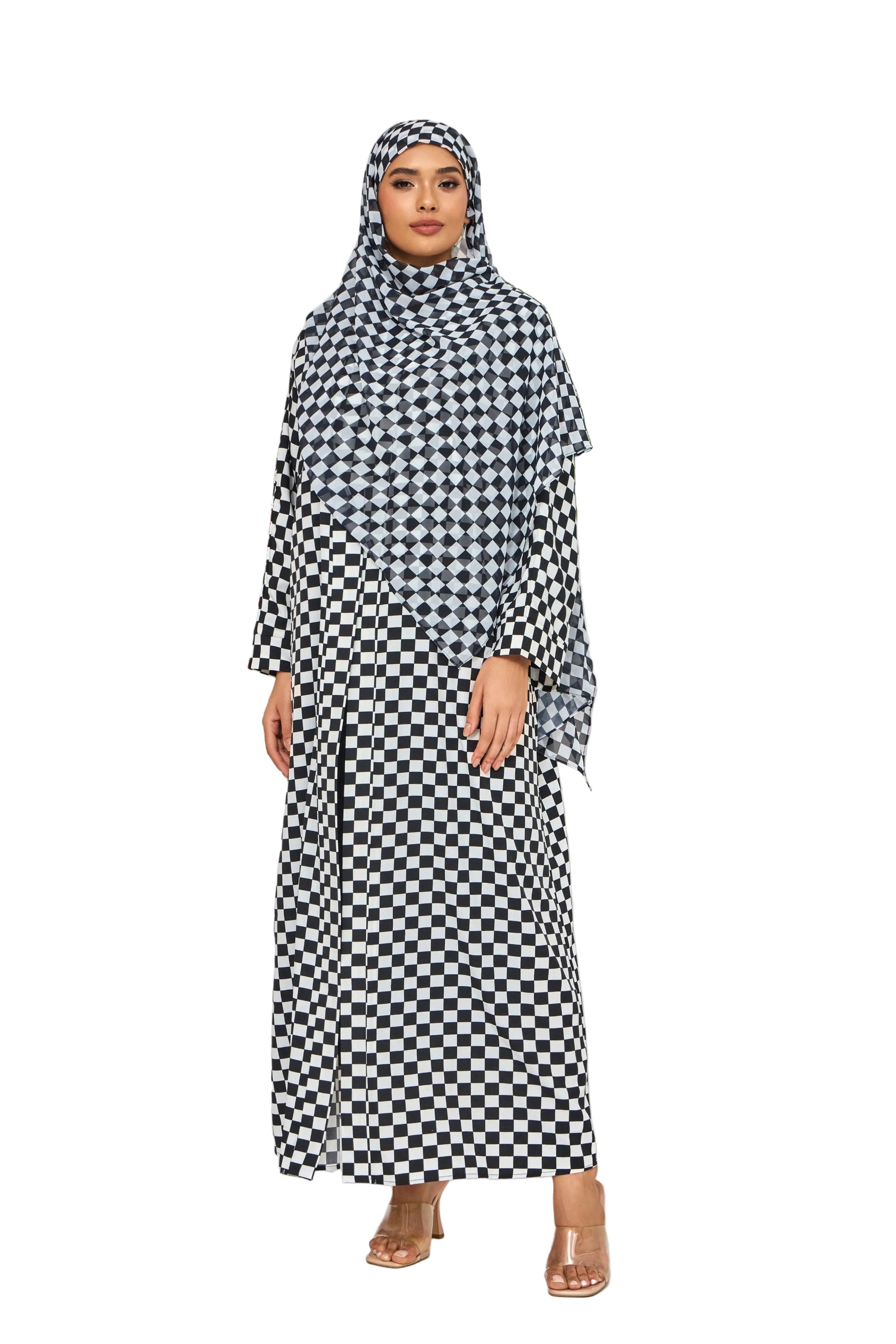 Woman wearing a black and white checkered abaya with matching hijab in a decorative setting with flowers and plants.